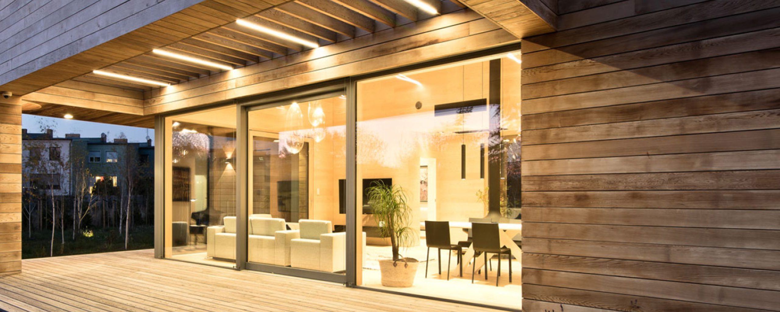 Wohnhaus mit großflächiger Fensterfront und Holzterrasse am Abend
