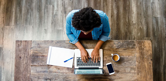 Person arbeitet mit Laptop an einem Massivholztisch